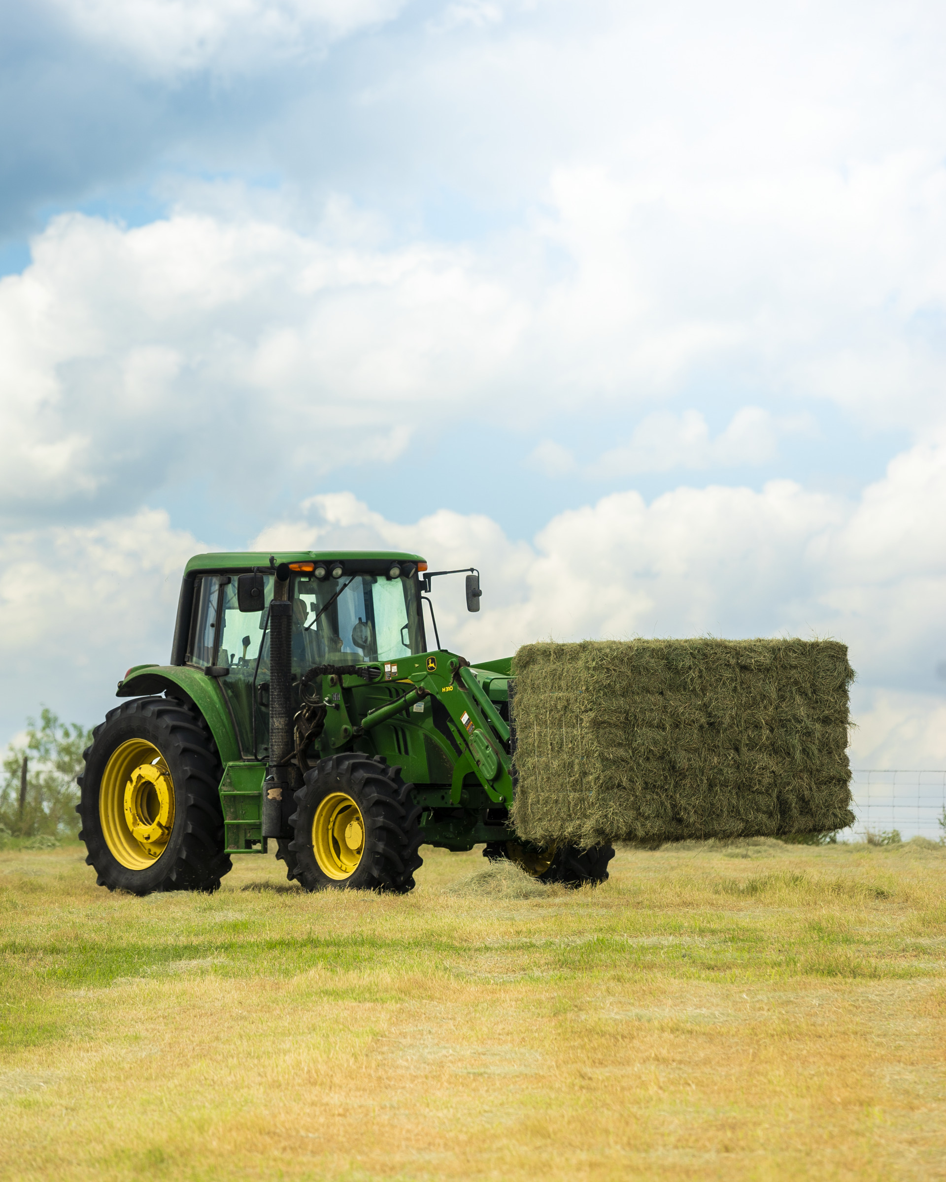 A John Deere tractor lifts a square bale of hay.
