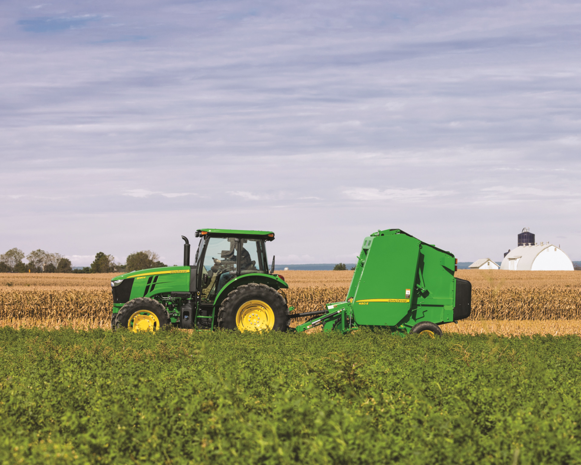 A John Deere tractor with a round baler attachment in a field in Texas.