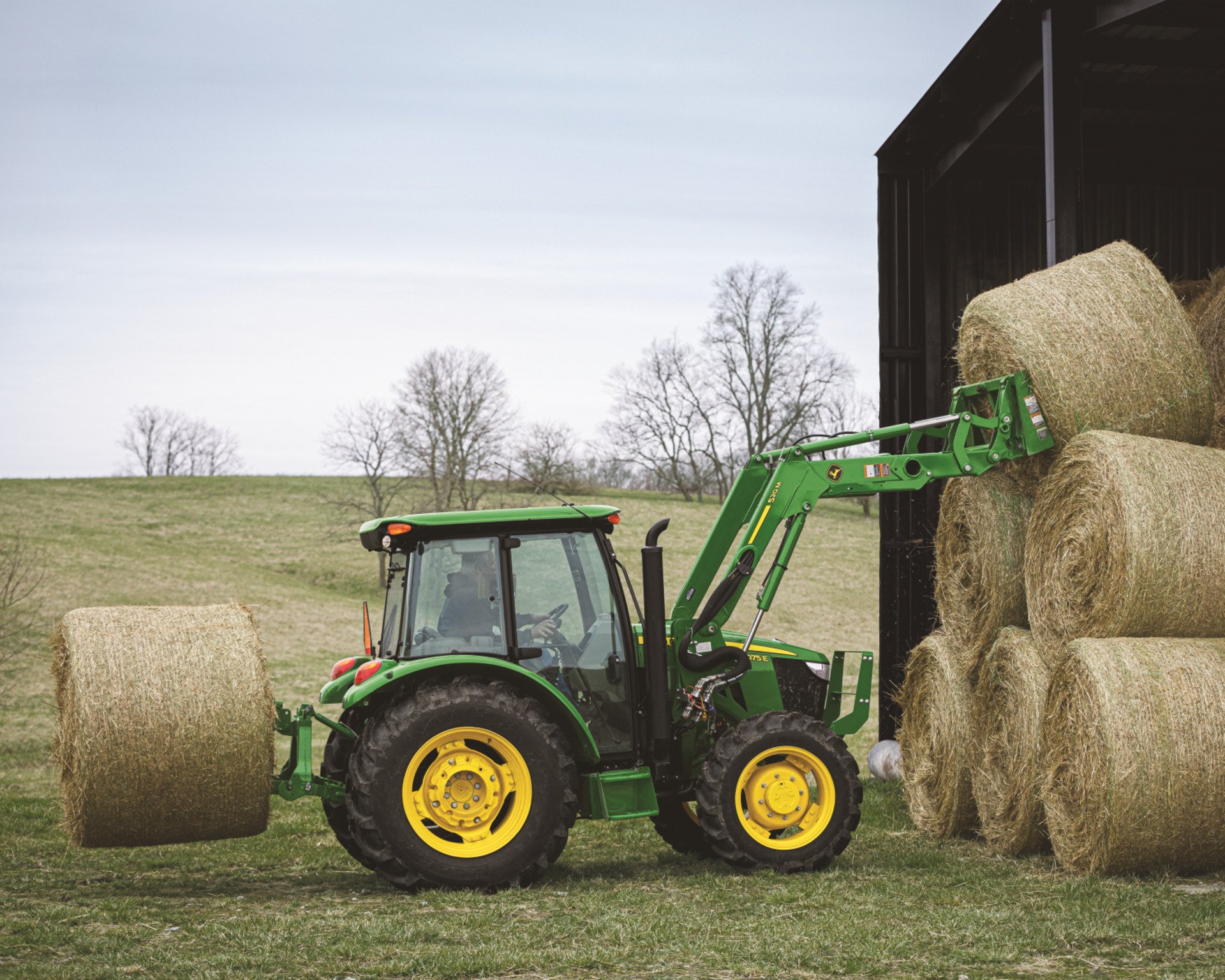 A John Deere tractor lifts hay bales to place them in a barn on a Texas farm.