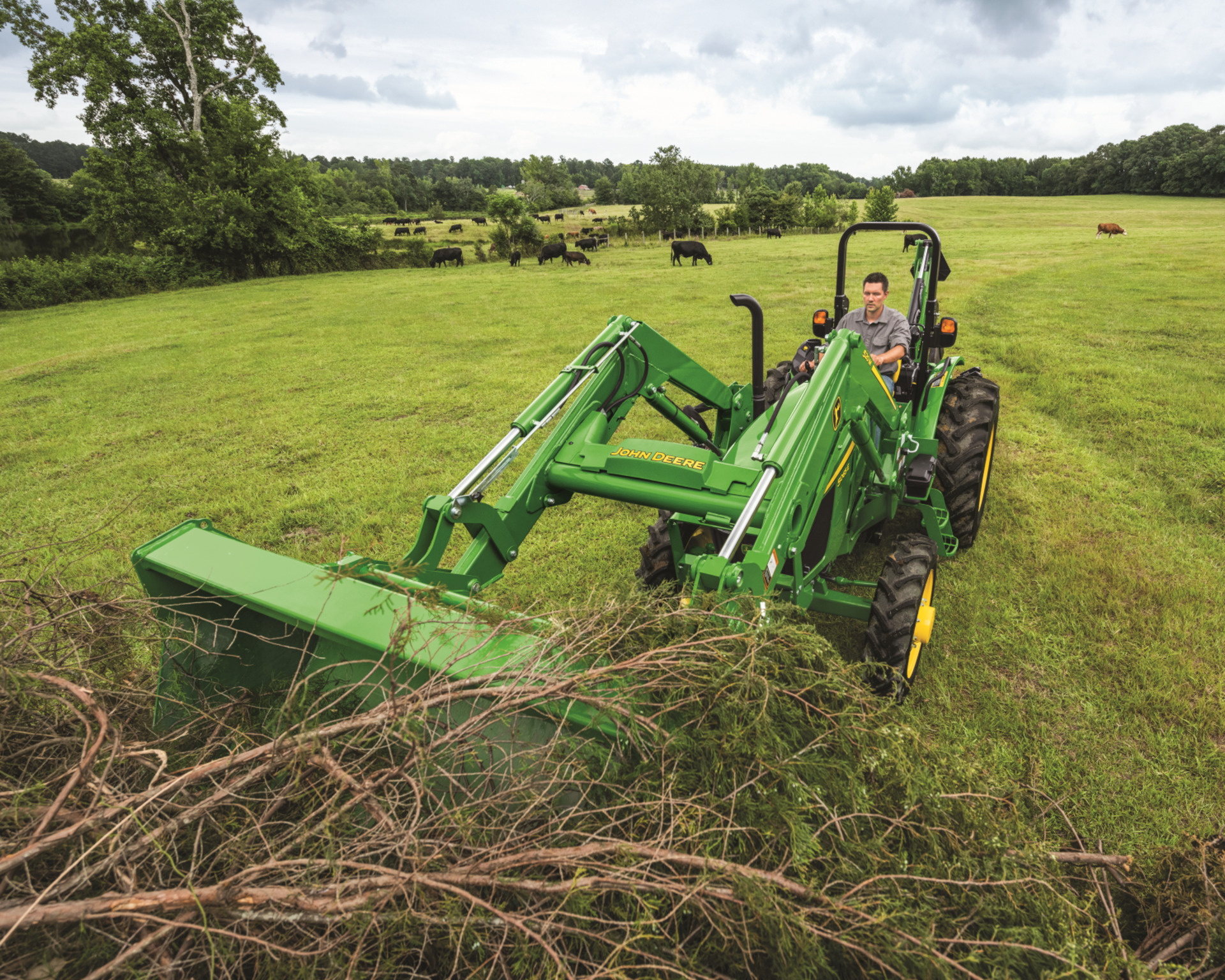 A man with a John Deere tractor moves brush with a front-end loader attachment.