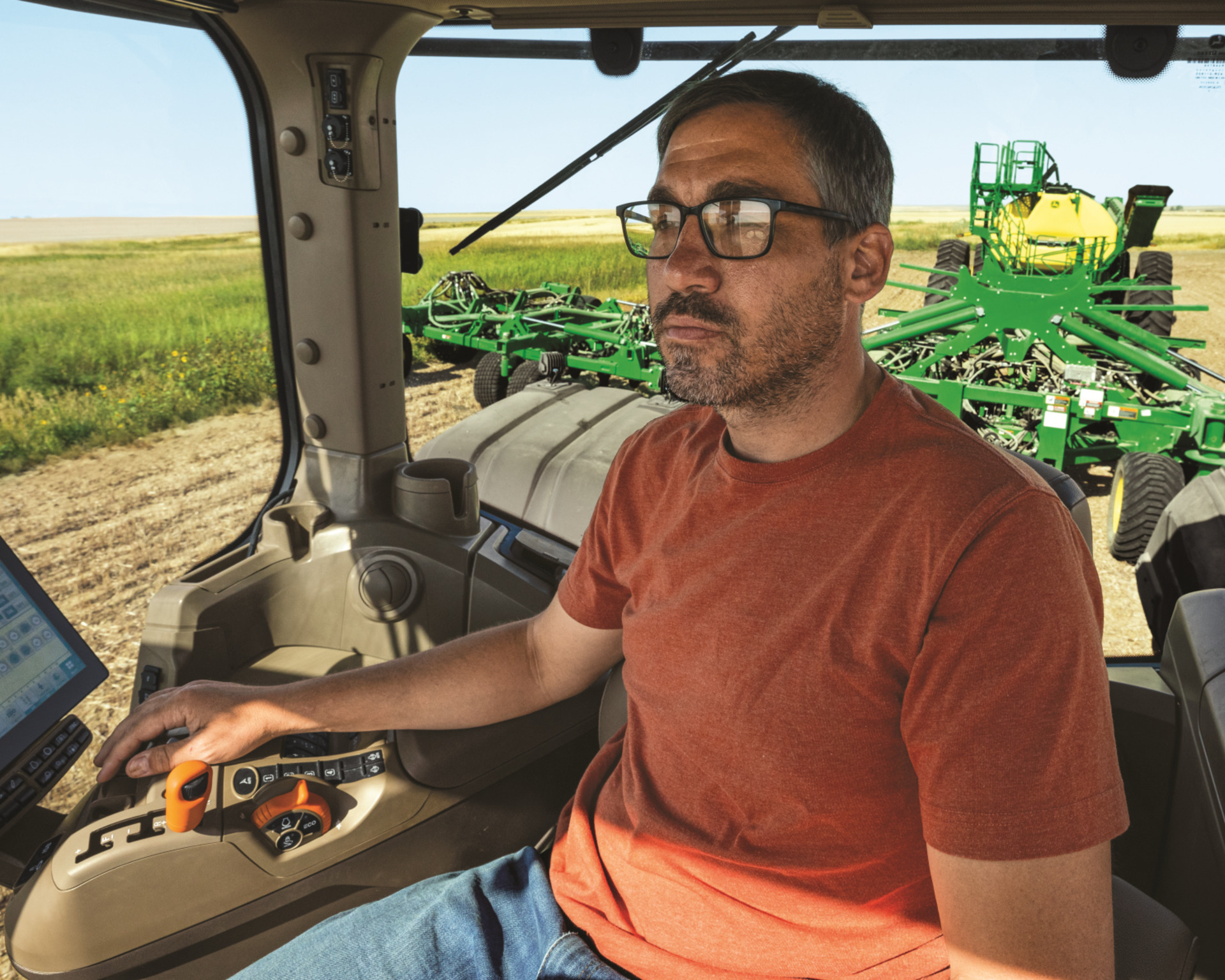 A tractor operator works inside the cab of a John Deere 9RX.