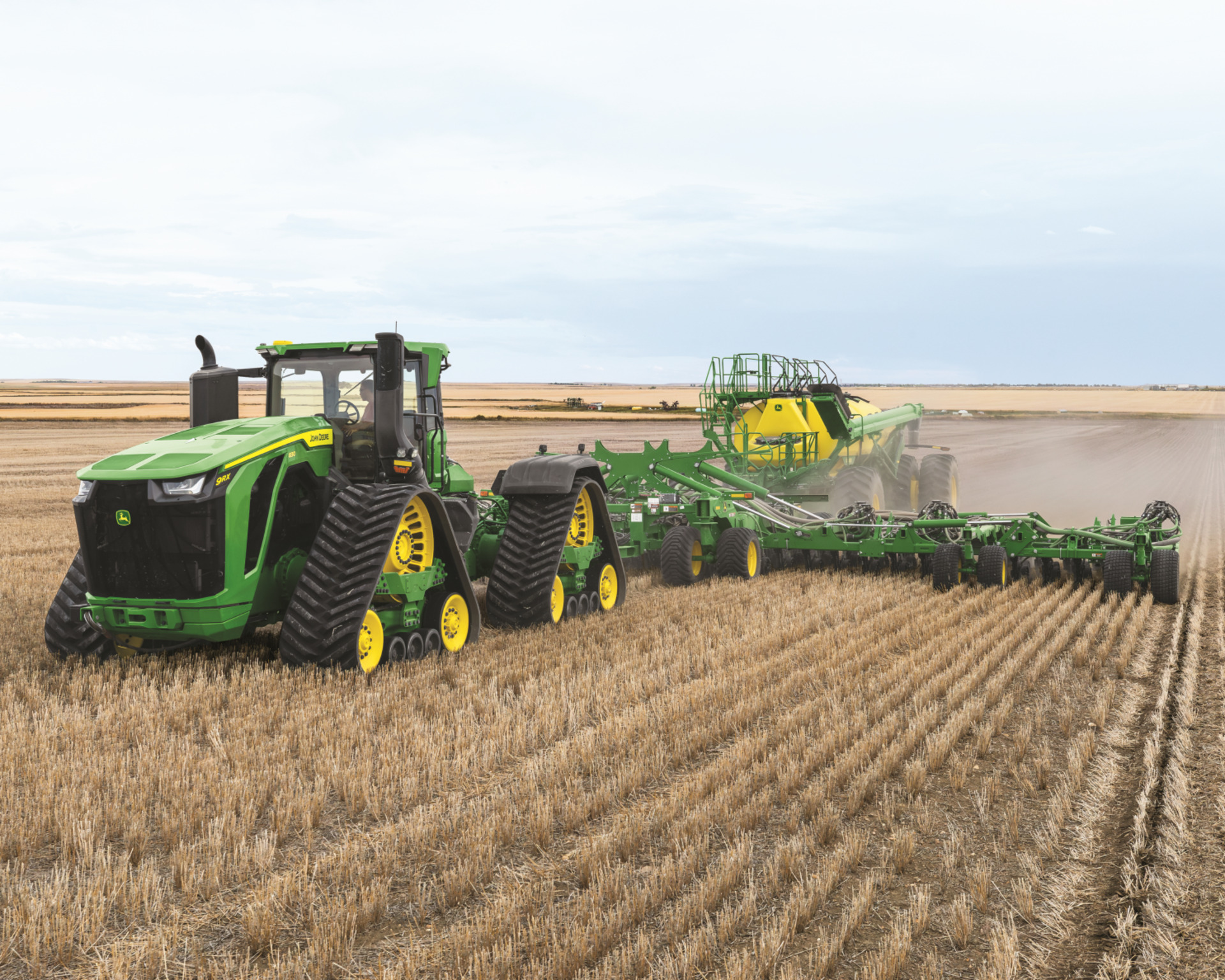 A John Deere 9RX track tractor pulls an attachment in a field.