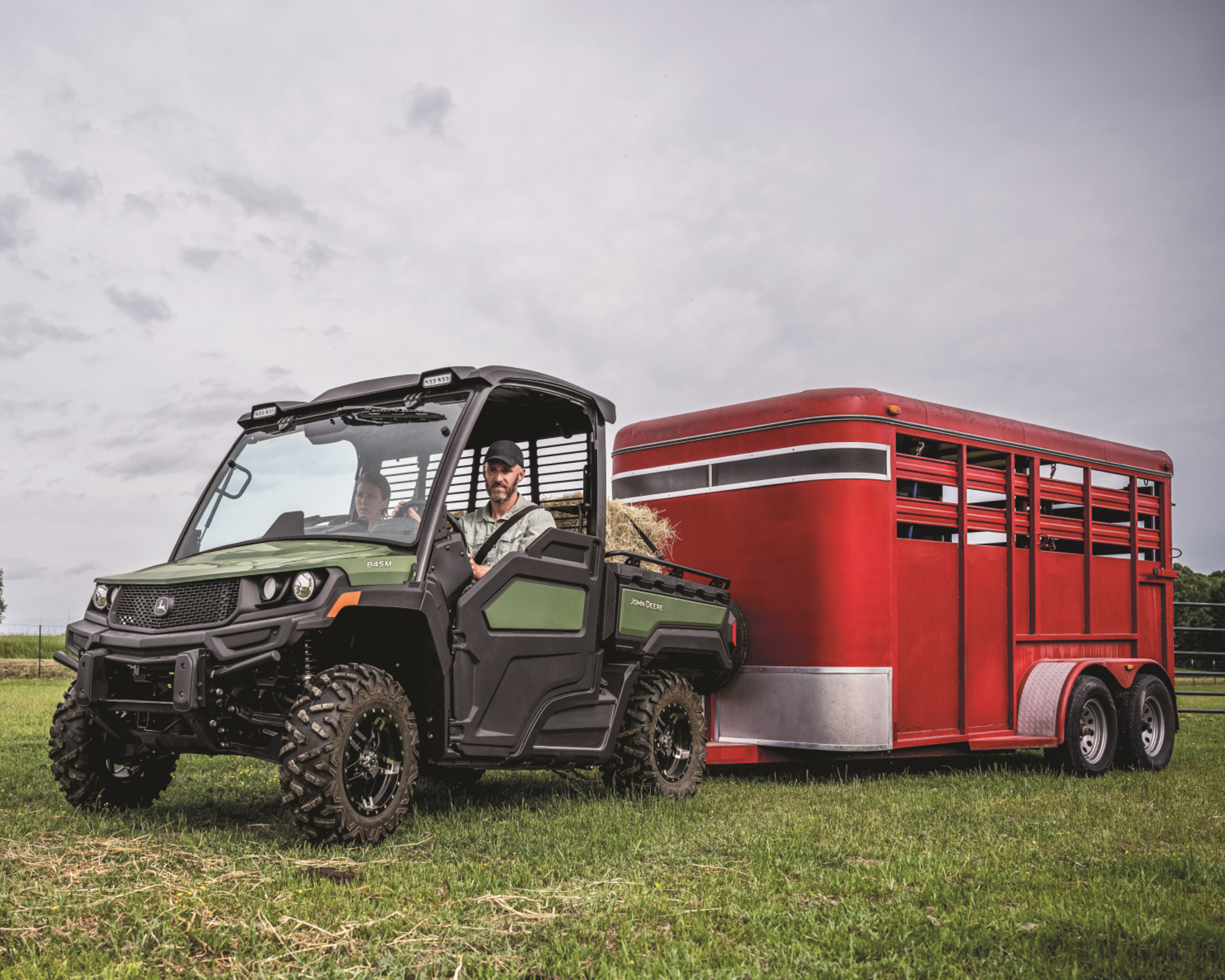 A farm worker pulls a livestock trailer with a John Deere Gator.