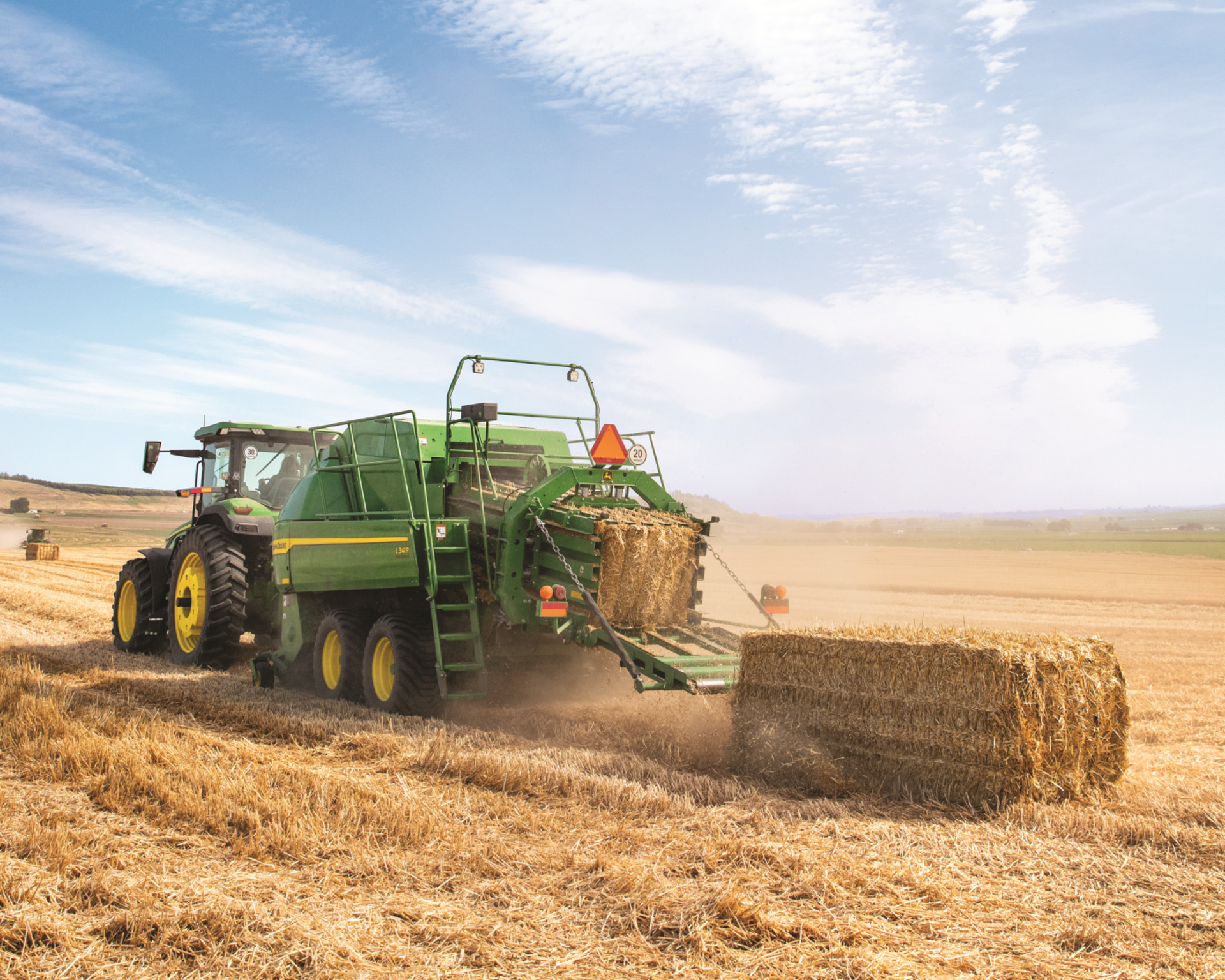 A tractor pulls a large square baler behind it in a field in Texas.