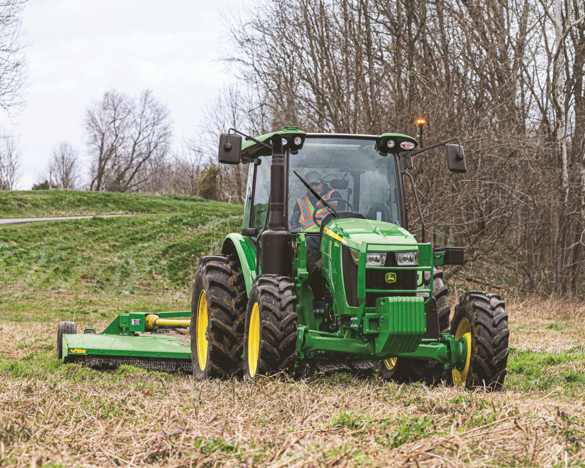 A worker operates a used tractor with a rotary cutter attachment.