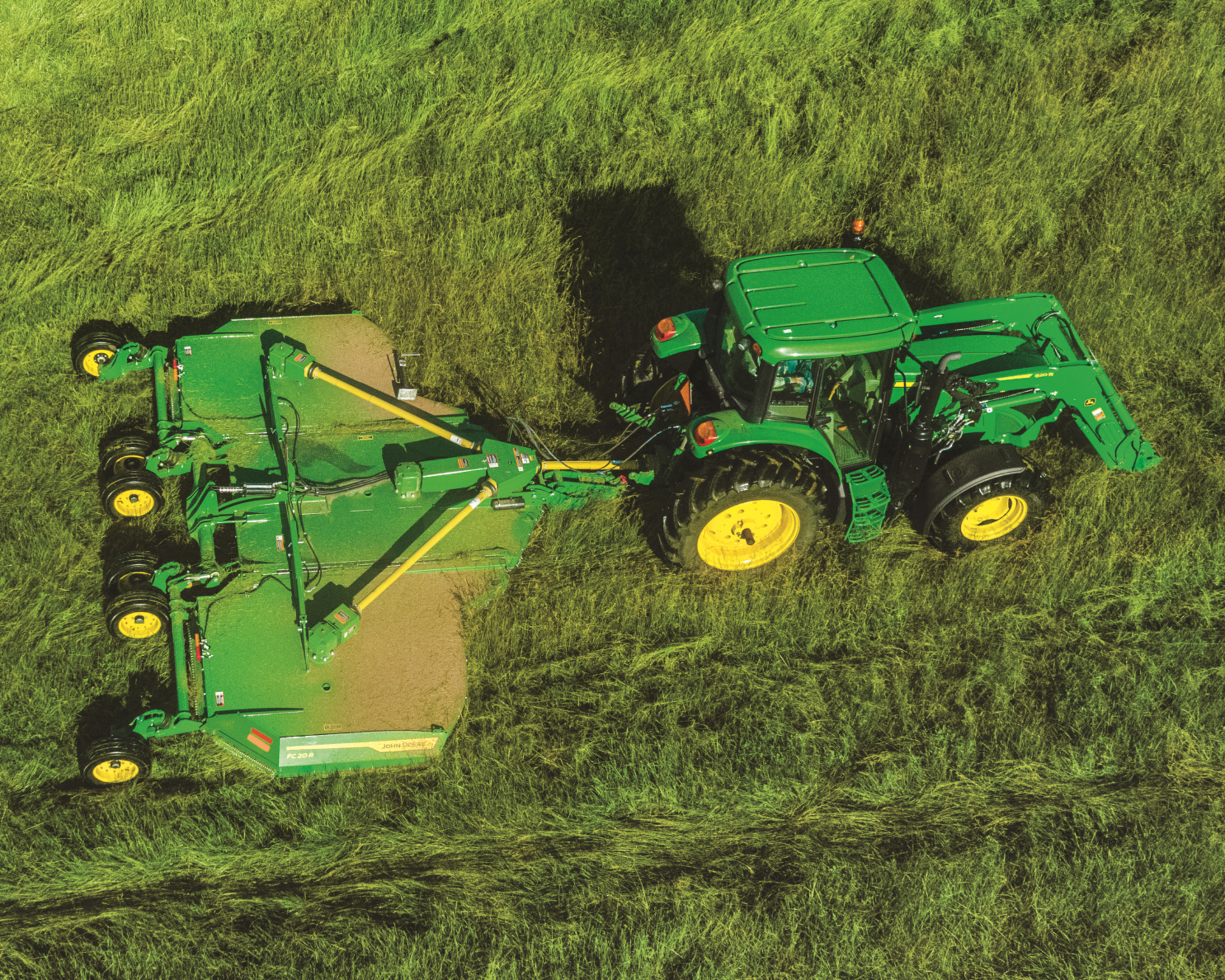 A John Deere tractor with a rotary cutter attachment clears tall grass in a field.