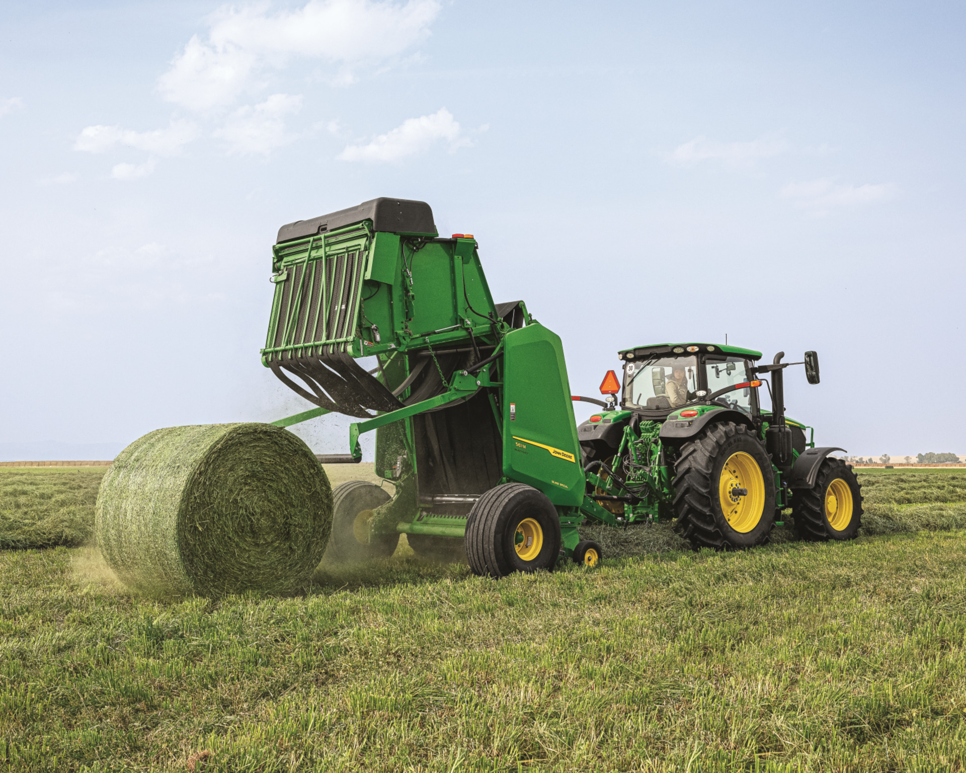 A round baler ejects a perfectly formed bale using a John Deere round baler attachment.