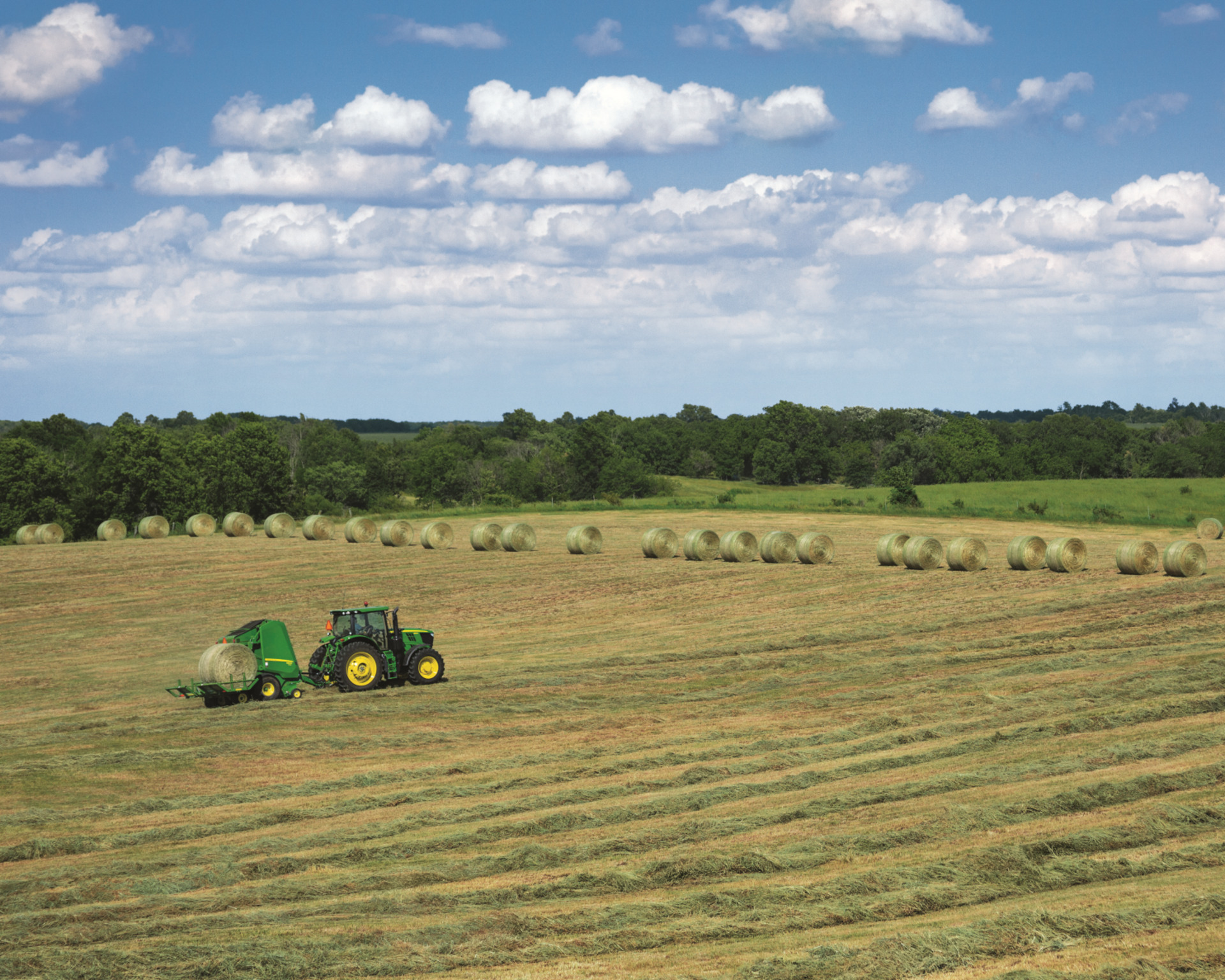 A John Deere tractor works a hay field in Texas with a John Deere round baler attachment.