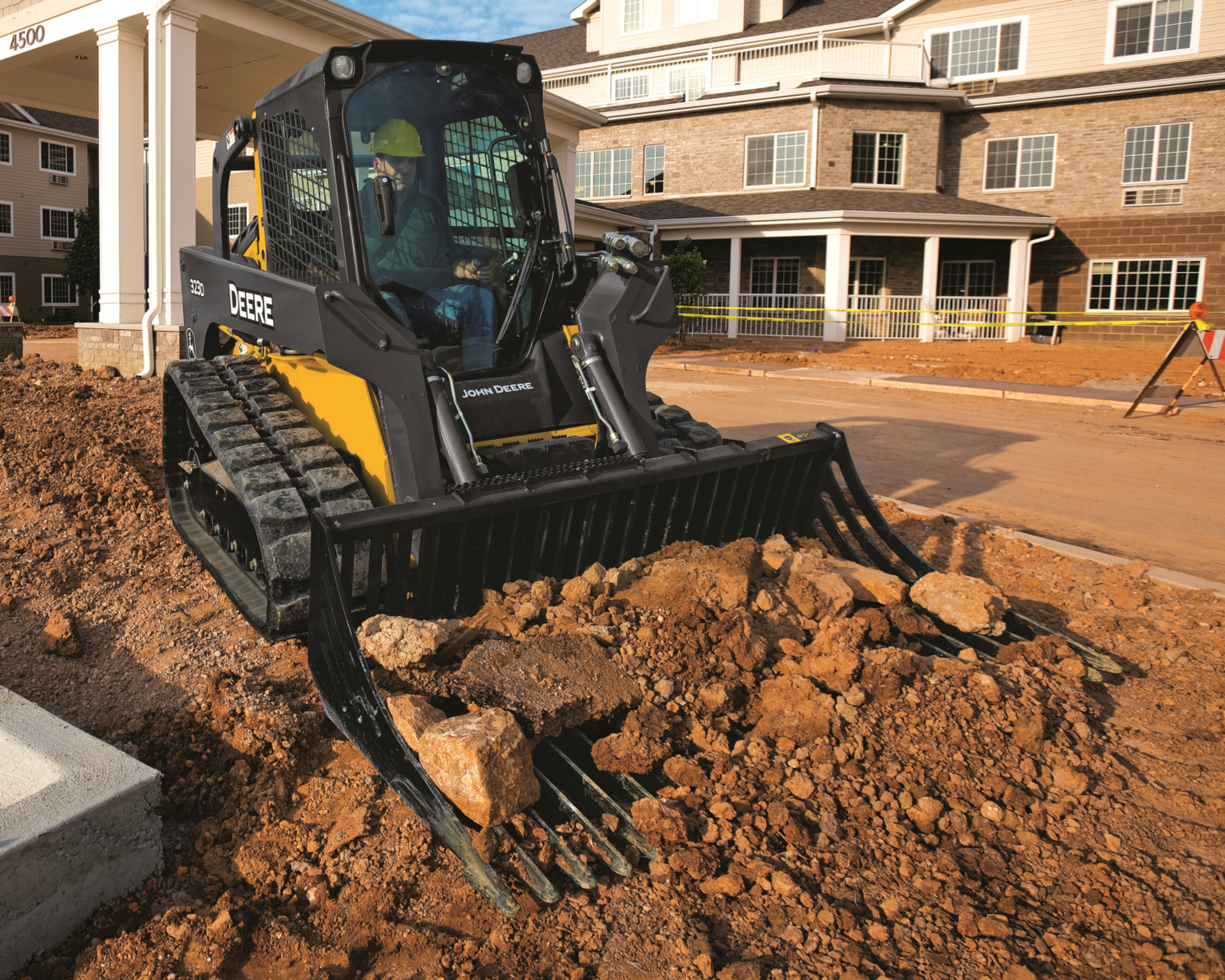 A compact track loader uses a bucket attachment to lift rocks and soil on a construction site.