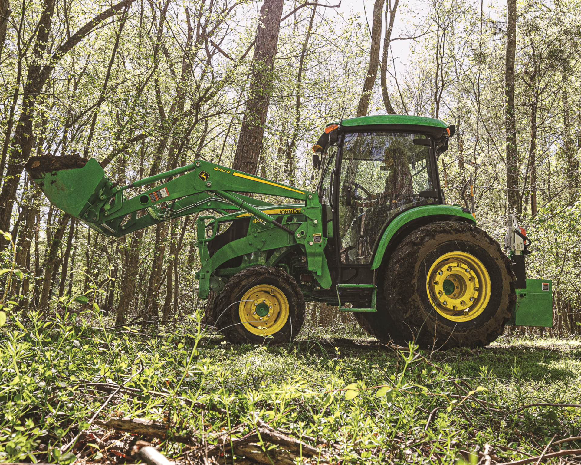 A John Deere tractor with a front-end loader lifts soil for a food plot.