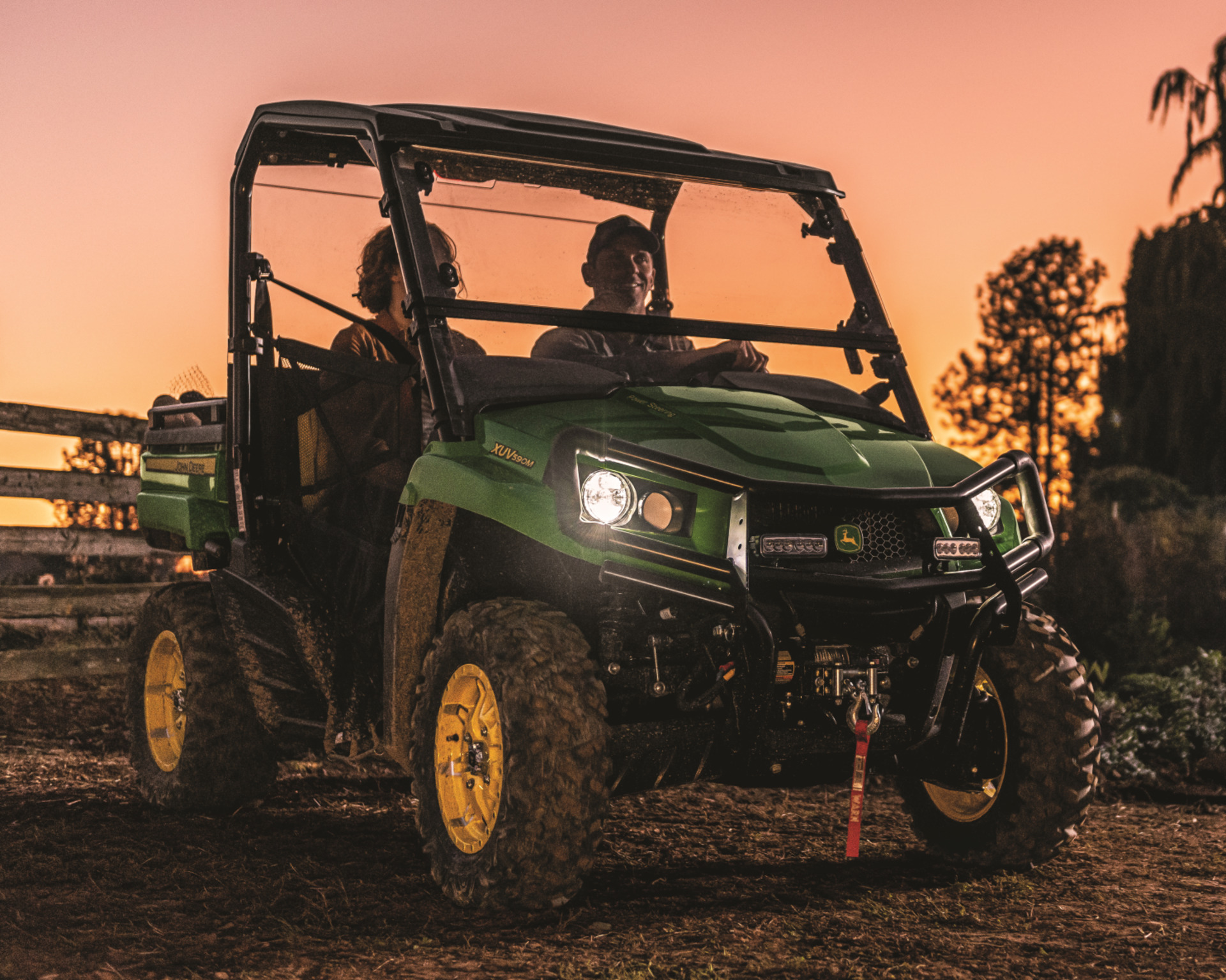 A Gator drives on a farm while the sun sets behind it.