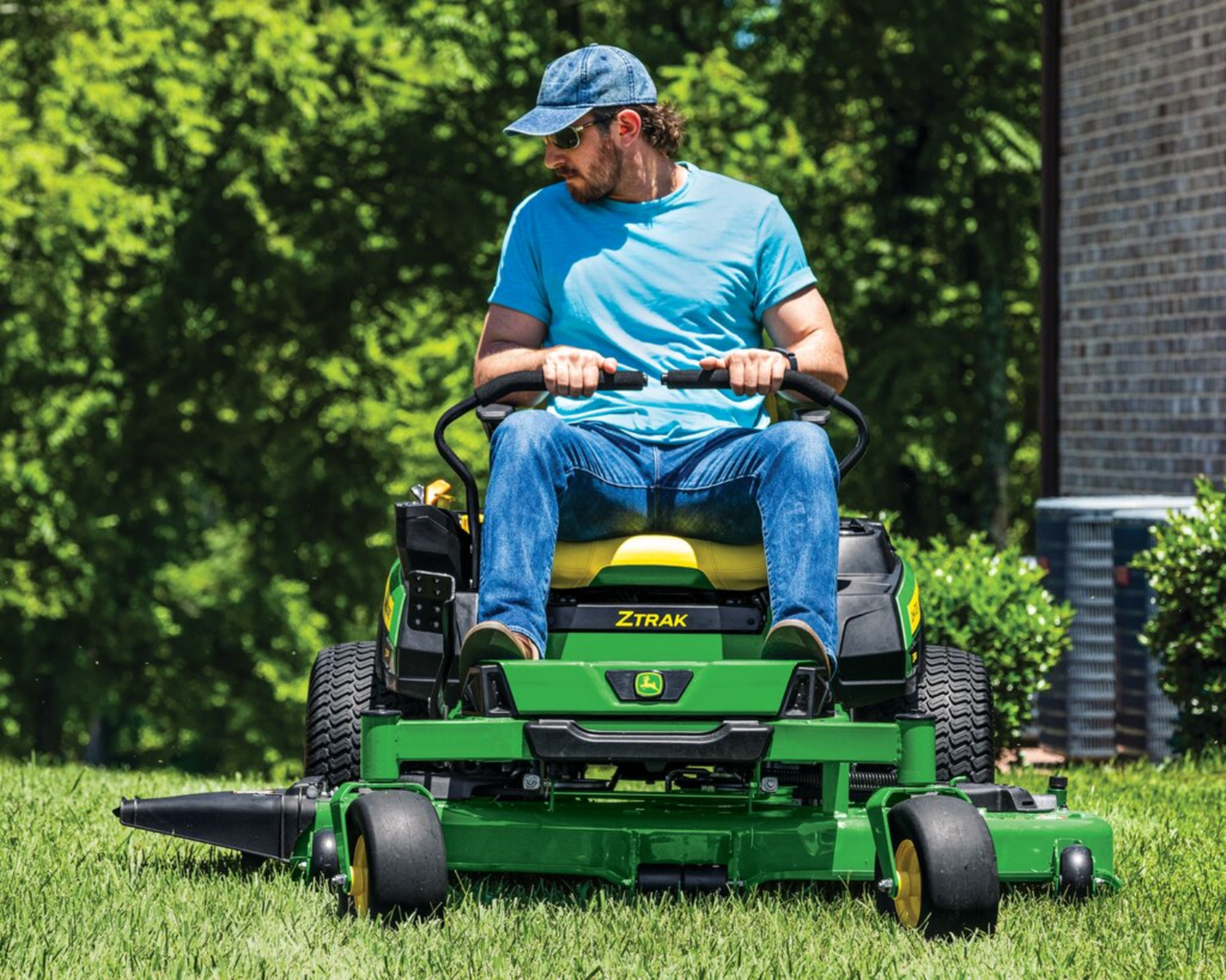 A man mows his lawn with a John Deere zero-turn mower.
